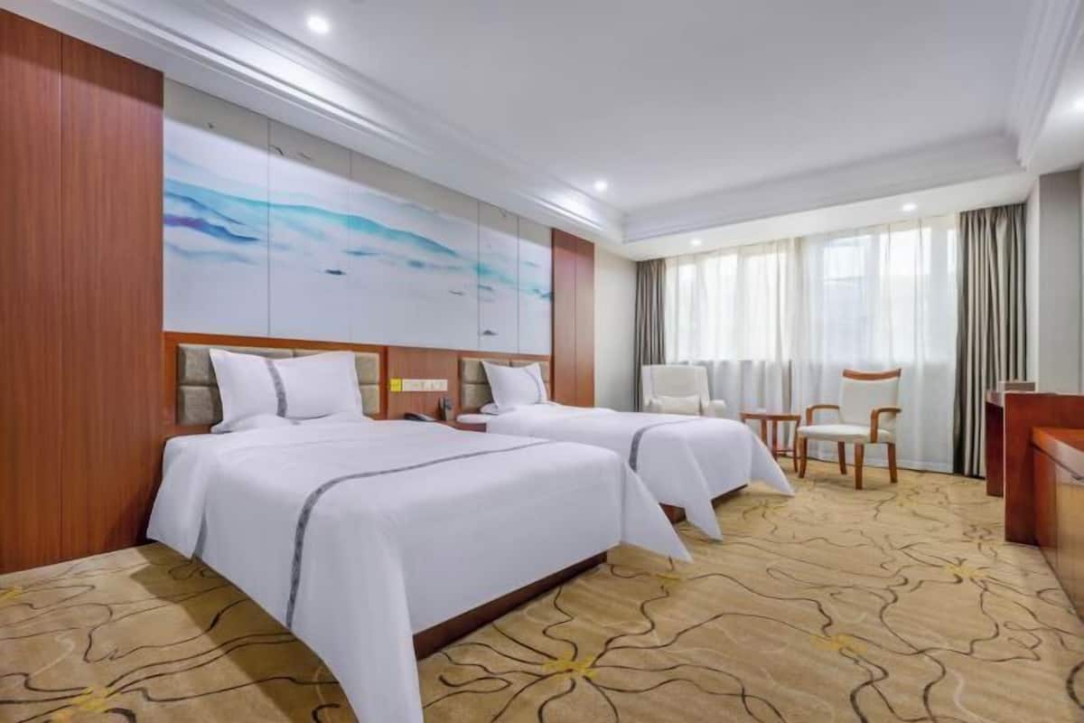 A hotel room with two beds, a desk, a chair, and a large abstract painting on the wall.