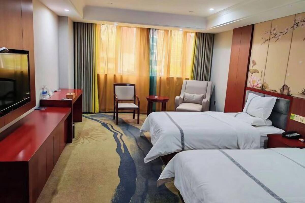 A hotel room with two beds, a desk, a chair, a television, and a window with curtains.