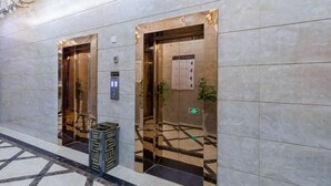 Ein Innenraum eines Hotellobbys mit zwei Aufzügen, Marmorboden und einer Dekoration an der Wand.