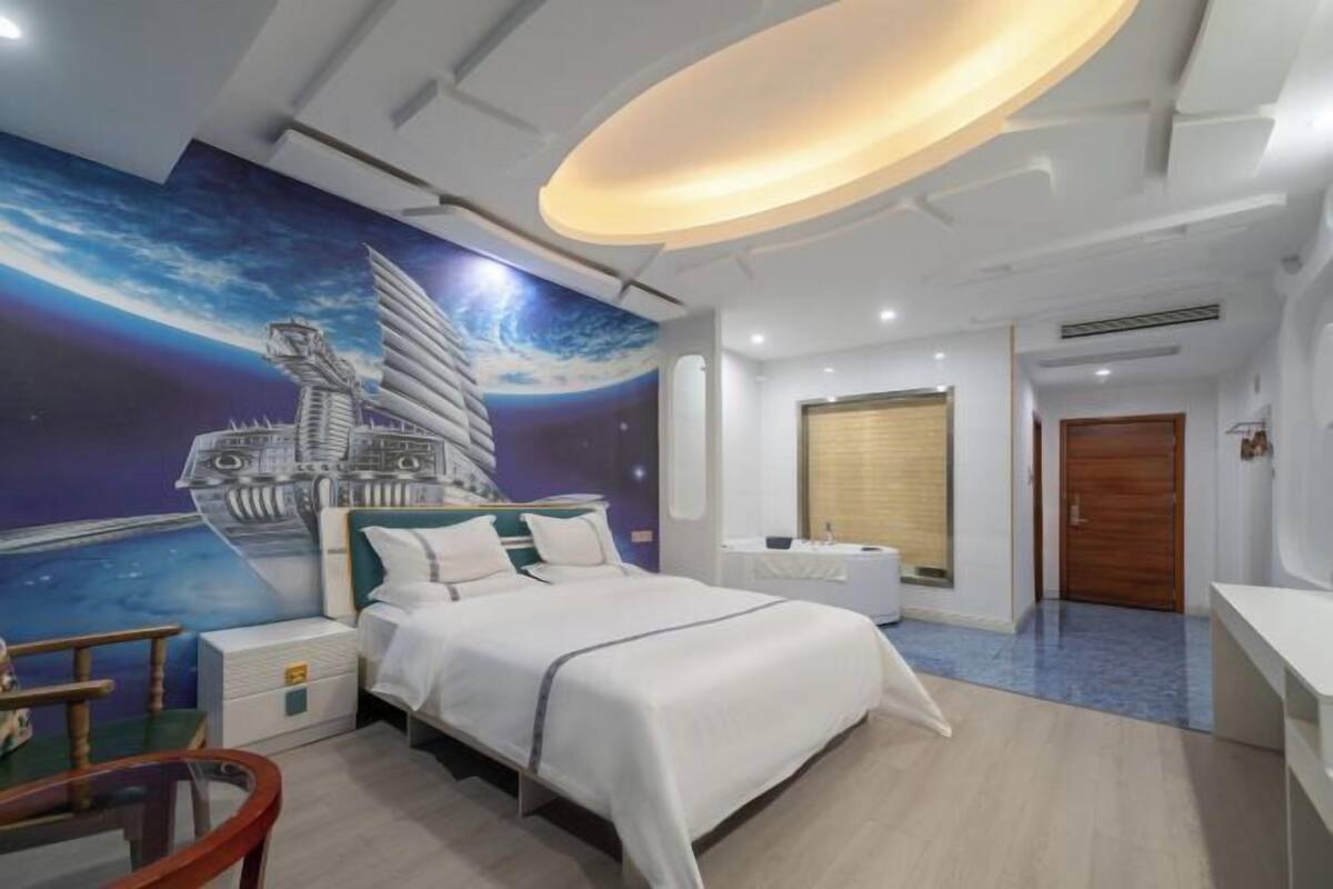 A modern hotel room with a bed, a desk, a chair, a window, and a wall mural.