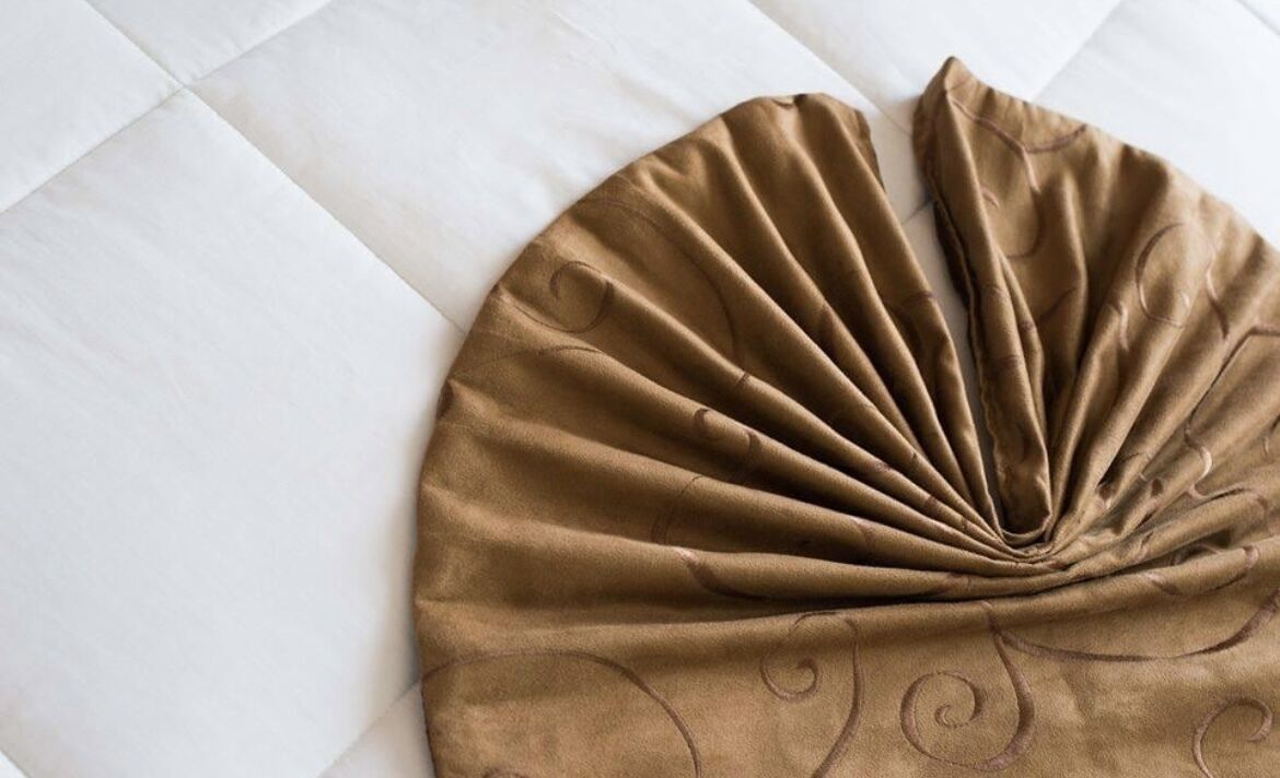A bed with a white quilt and a brown decorative pillow.