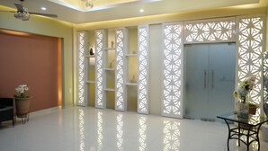 A spacious room with a high ceiling, a ceiling fan, a glass table with a chair, a potted plant, and a decorative white partition with geometric patterns. - Ivissa Hotel  (Pinotepa Nacional)