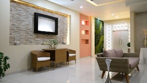 A modern lobby with a wall-mounted TV, wicker furniture, a green vertical garden, and a decorative white vase. - Ivissa Hotel  (Pinotepa Nacional)