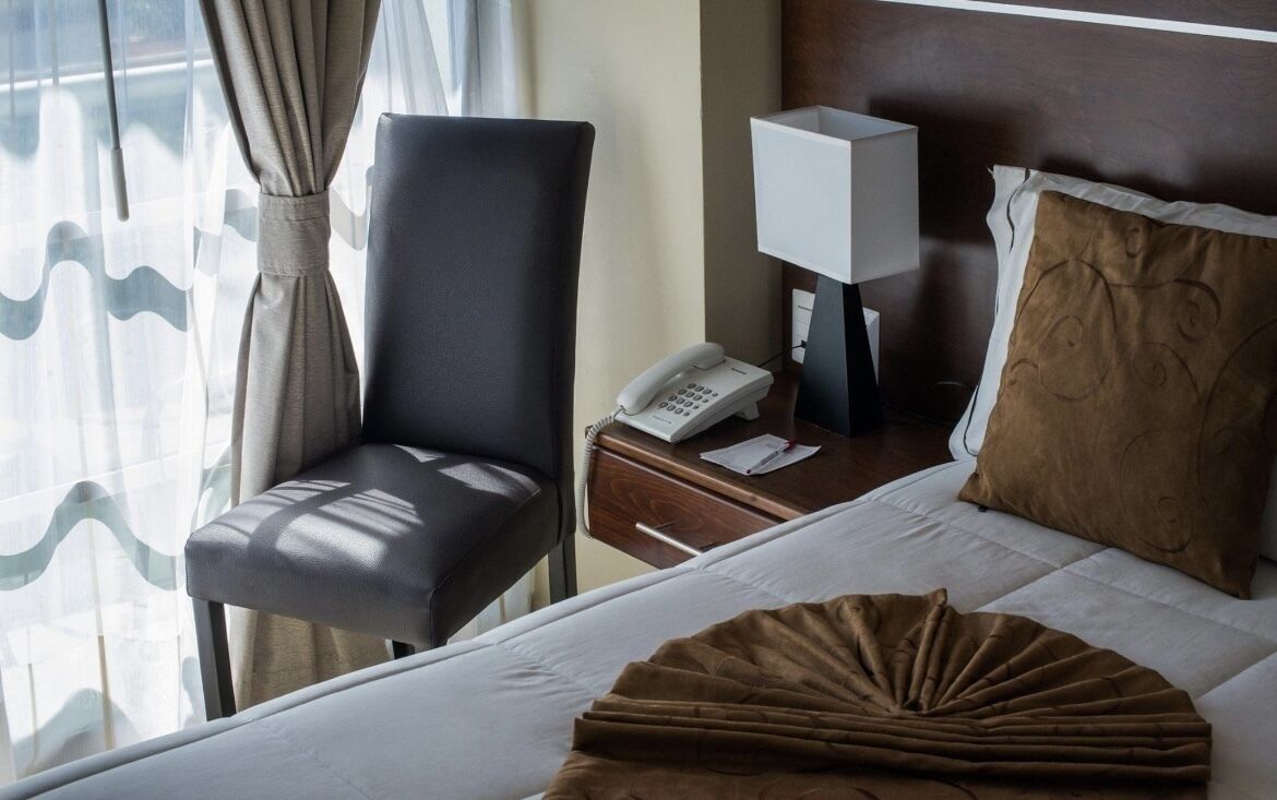 Una habitación de hotel con cama, una silla, mesita de noche con lámpara y teléfono.