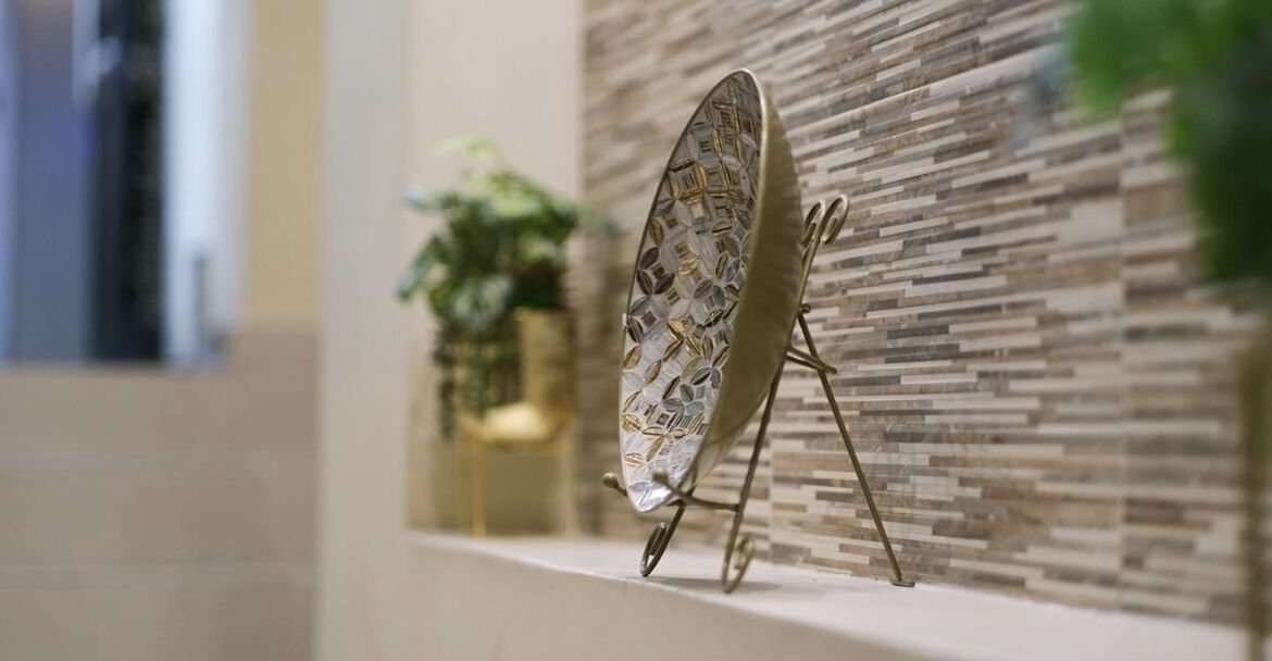 Un soporte de metal decorativo con un objeto con diseño sobre él, colocado sobre un repisa frente a una pared con textura.