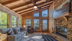 Un intérieur de chalet chaleureux avec un plafond en bois, de grandes fenêtres, une cheminée et un tapis moelleux.