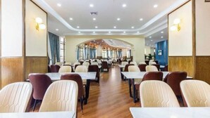 Un vaste espace dédié à la salle à manger, avec de nombreuses tables et chaises, un plafond haut doté d’un éclairage encastré, et une vue sur la salle à manger en arrière-plan.