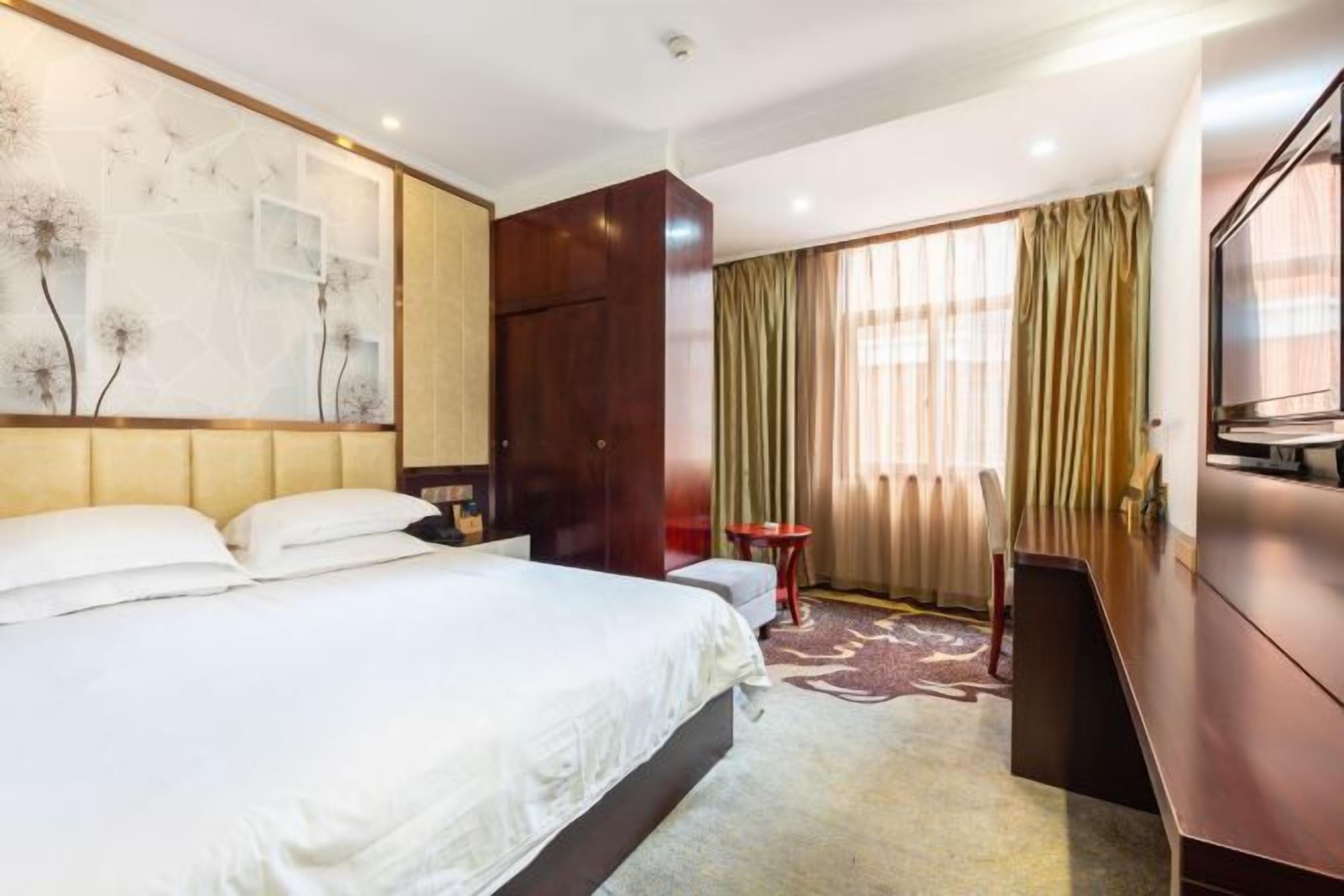 A hotel room with a large bed, a desk, a chair, and a TV.