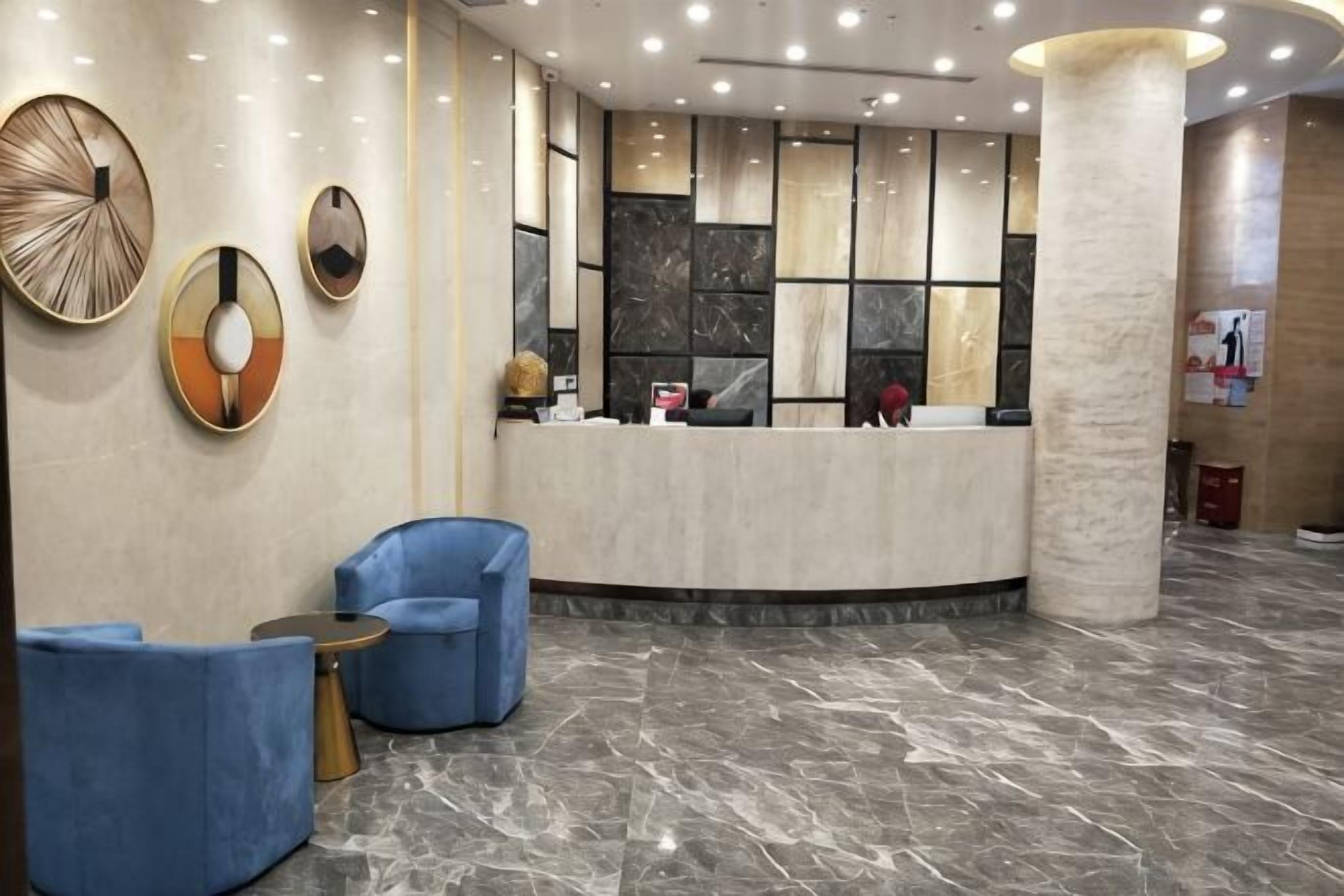 A hotel reception area with a marble floor, a reception desk, and blue armchairs.