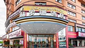 L’entrée d’un hôtel, avec une façade incurvée, des portes en verre et une enseigne multilingue.