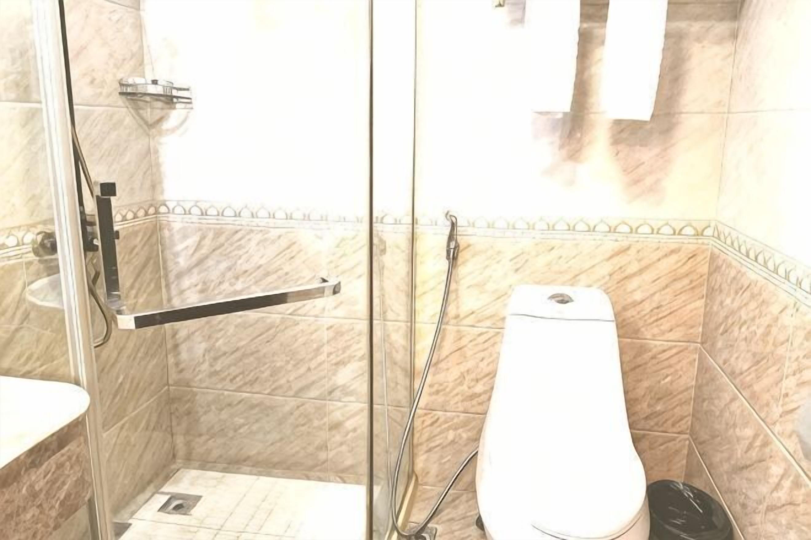 A bathroom with a glass shower enclosure, a white toilet, and a tiled floor.