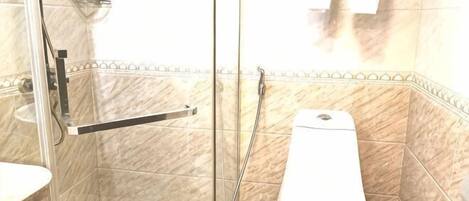 A bathroom with a glass shower enclosure, a white toilet, and a tiled floor.