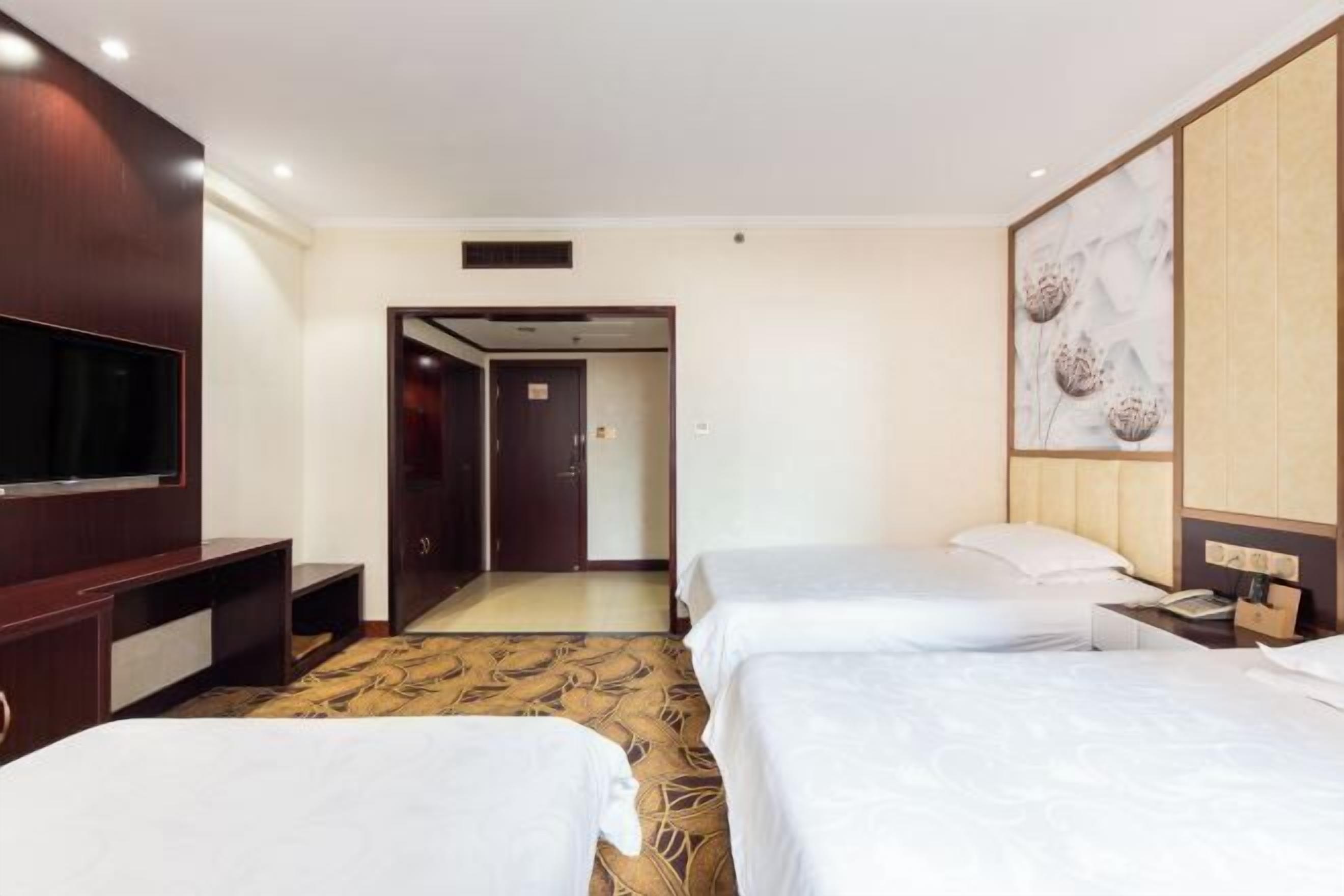 Una camera d'albergo con due letti, una televisione, una scrivania e uno specchio grande.