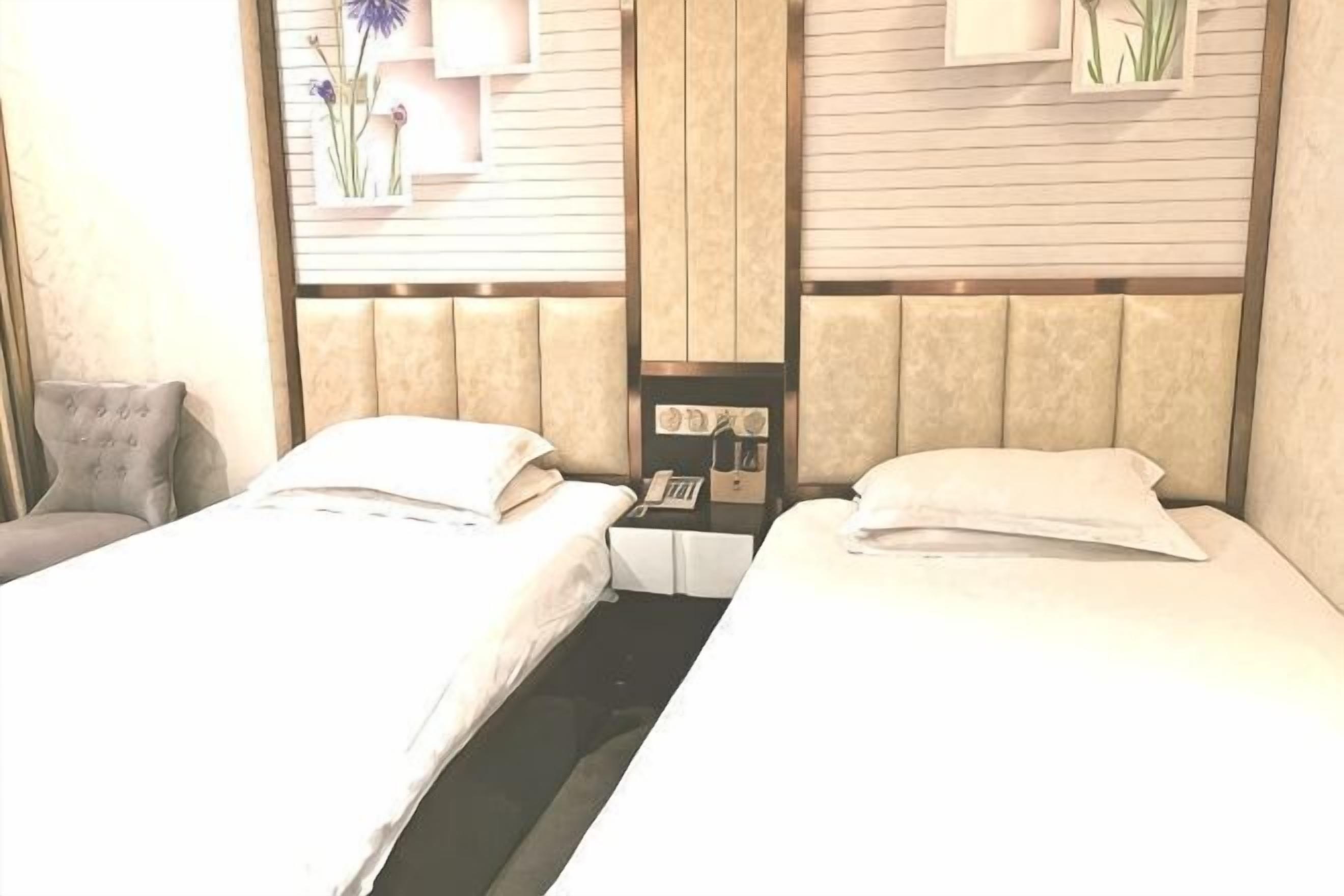 A hotel room with two beds, a nightstand with a phone, and a wall-mounted shelf with decorative items.