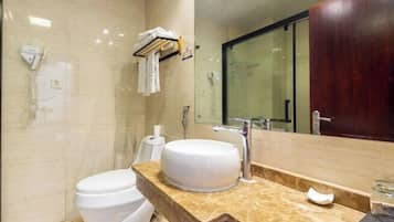 A modern bathroom with a white toilet, a large sink with a marble countertop, a glass shower enclosure, and a wooden vanity cabinet.