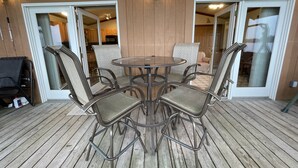 A covered patio with a round table and six chairs, wooden flooring, and sliding glass doors leading to an interior space.
