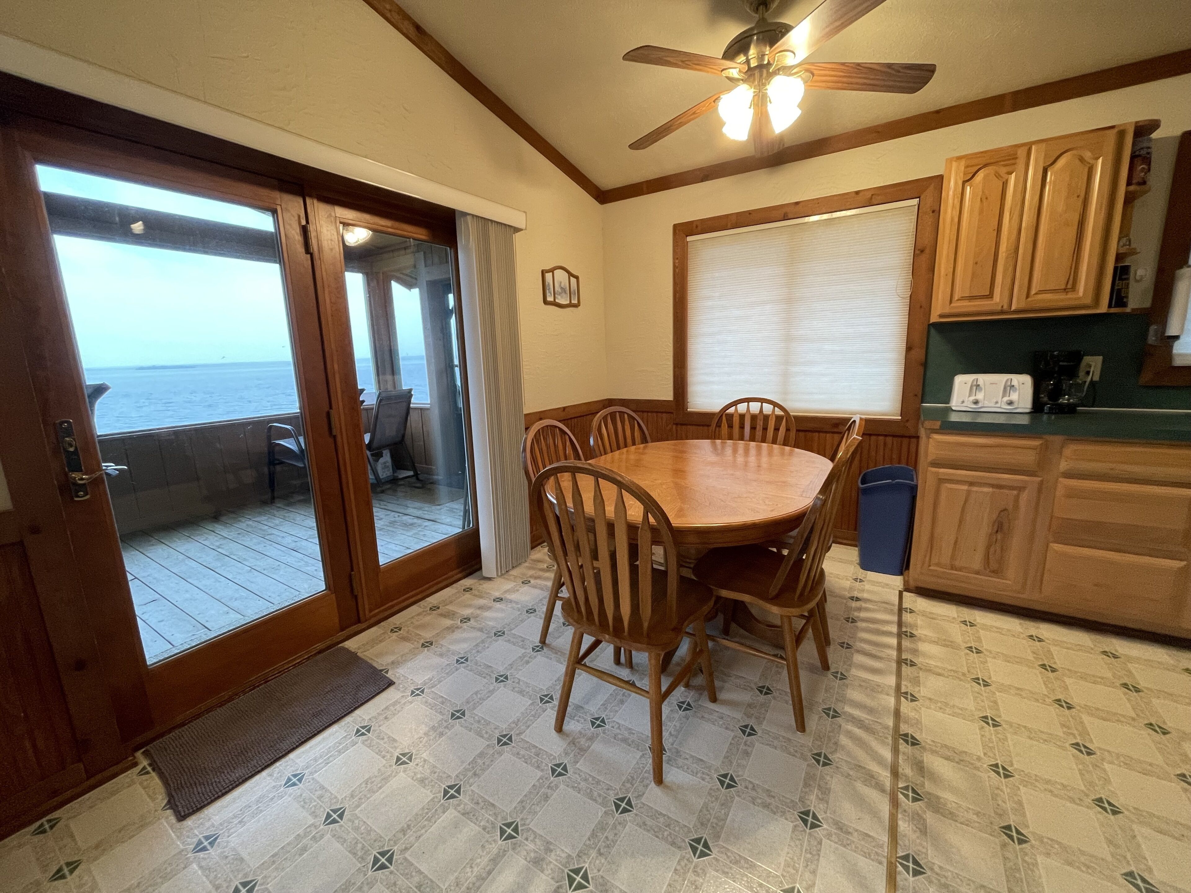 A compact kitchen with wooden cabinets, a dining table with chairs, a ceiling fan, and a view through a sliding glass door to the outside.