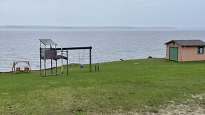 A grassy area with a swing set, a small shed, and a view of a body of water.