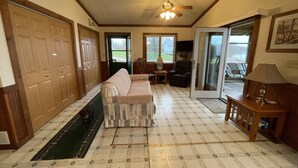 A spacious living area with a sofa, a coffee table, and a ceiling fan. There are wooden doors and a sliding glass door leading to an outdoor area.