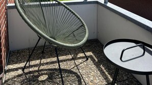 A balcony with a green wire chair and a small round table, overlooking a residential area with houses and greenery. - Schöne 3 Zi. Whg im Surflook in der Nähe der Familienlagune (Büsum)