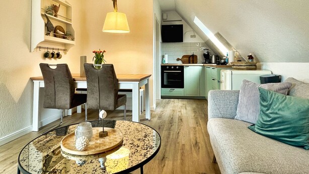 A compact living space with a dining area, kitchenette, and a sofa. - Schöne 3 Zi. Whg im Surflook in der Nähe der Familienlagune (Büsum)