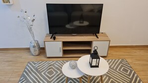 A modern living room with a flat-screen TV on a wooden TV stand, a small side table with a decorative item, and a patterned rug on the floor. - Premiere apartment near the financial center of San Isidro (Lince)