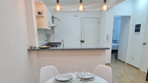 A modern dining area with a round table set for four, white chairs, and pendant lighting. - Premiere apartment near the financial center of San Isidro (Lince)