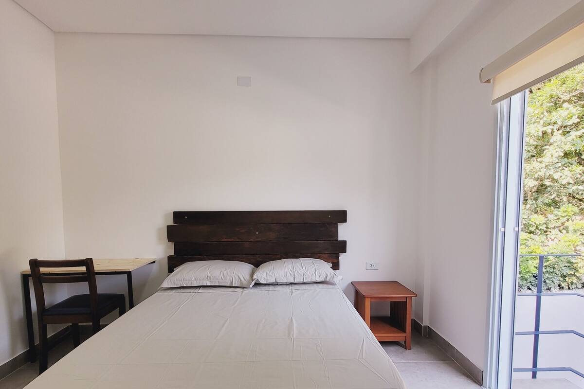 A bedroom with a large bed, a wooden nightstand, a small table, and a chair.