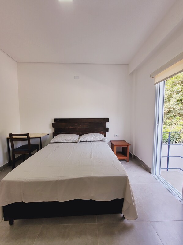 A bedroom with a large bed, a wooden nightstand, a small table, and a chair.