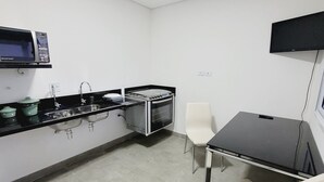 A kitchenette with a microwave, sink, and stove, a small table with two chairs, and a TV mounted on the wall. - Mimos Hospedagem (São Paulo)