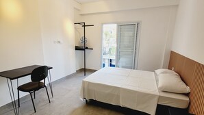 A modern bedroom with a bed, a desk, and a chair. There is a window with blinds, a ceiling fan, and a power outlet on the wall. - Mimos Hospedagem (São Paulo)