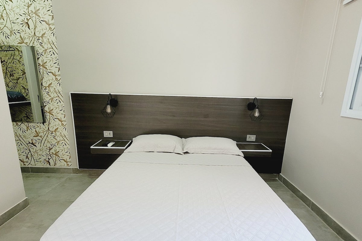 A bedroom with a bed, a nightstand, a wall-mounted lamp, and a mirror.