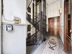 Un couloir avec un escalier, une porte et un clavier de sécurité.