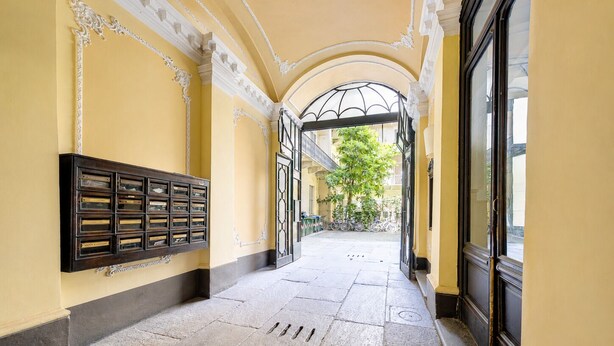 A corridor with a stone floor, a metal gate, and a wall-mounted display case.
