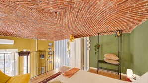 A room with a brick ceiling, a bed with pillows, a hanging chair, and a view through a window.