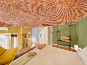 Una stanza con soffitto in mattoni, un letto con cuscini, una poltrona sospesa e vista dalla finestra.