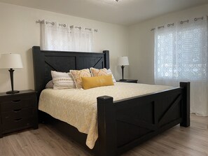 Une chambre à coucher bien rangée, avec un cadre de lit en bois foncé, deux tables de chevet dotées de lampes et une couvre-lit à motifs.