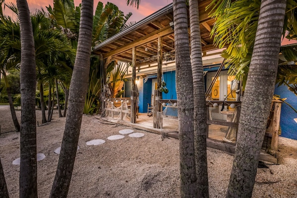 Ein Gebäude am Strand mit einer Holzterrasse, umgeben von Palmen und Sand.