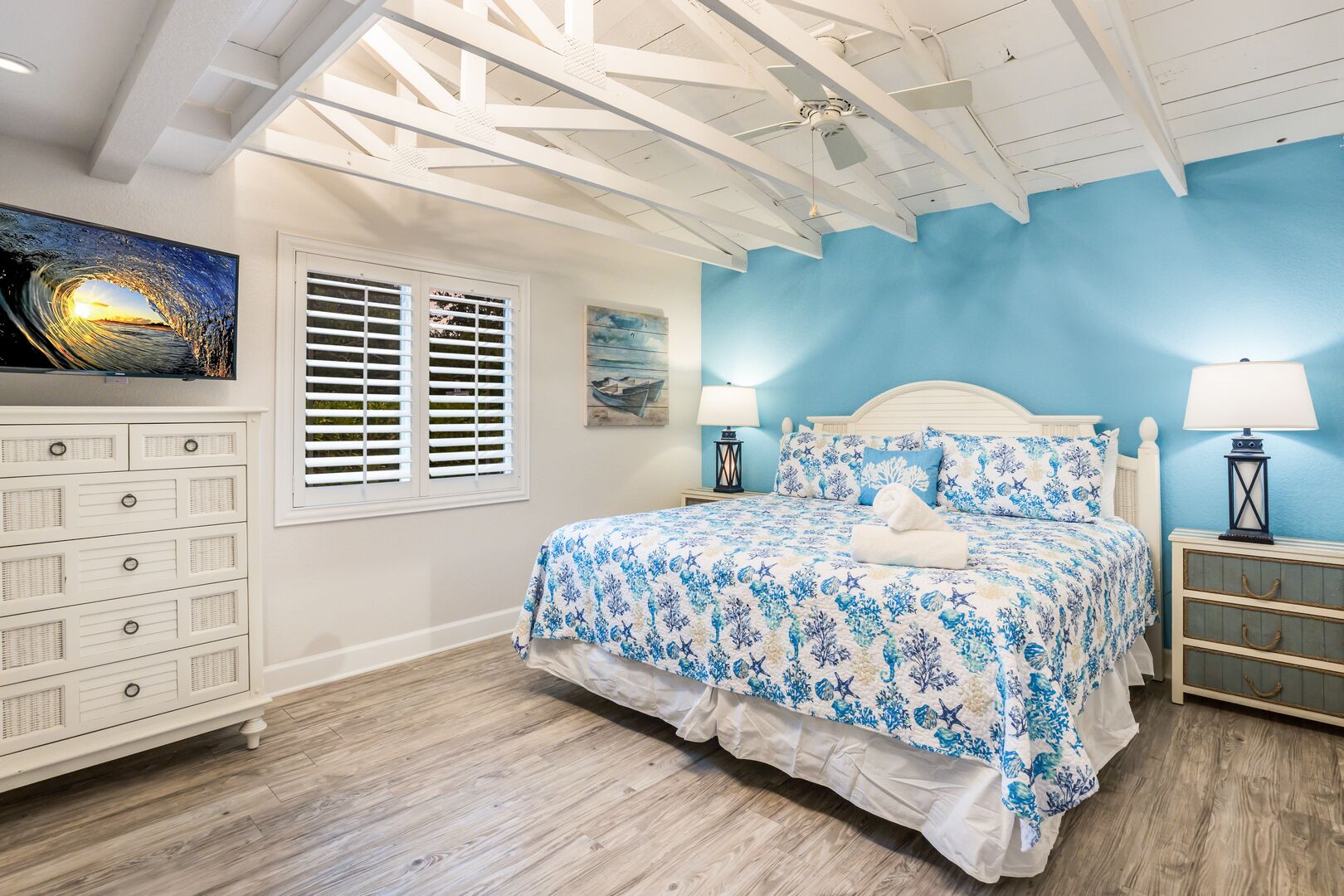 A bedroom with a bed, a dresser, a window with shutters, and a ceiling fan.