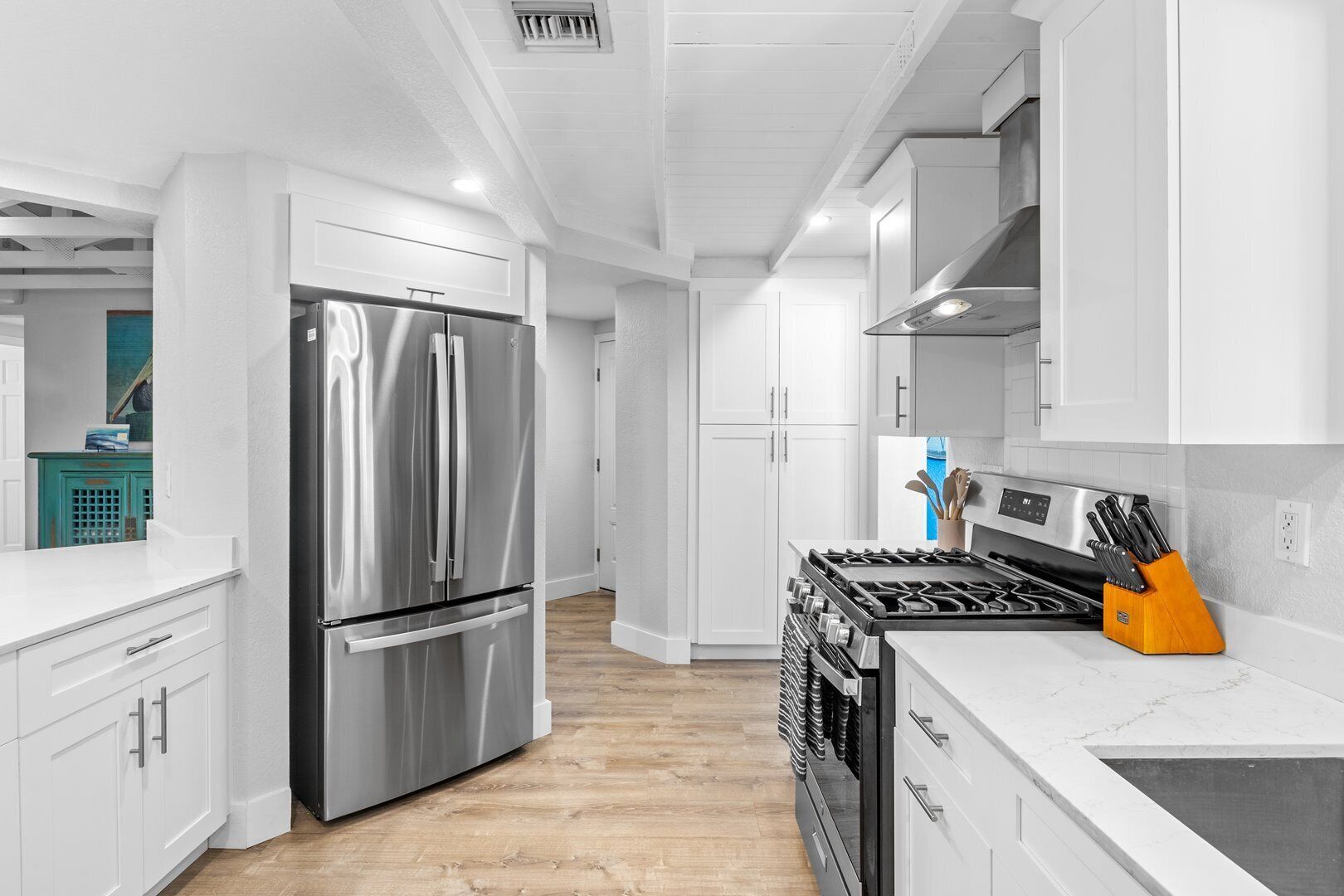 A modern kitchen with white cabinetry, stainless steel appliances, and a wooden floor.