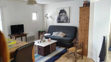 A living room with a dark blue sofa, a wooden chair, a small table with a lamp, a television, and a window.