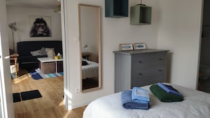 A bedroom with a bed, a dresser, a desk, a chair, a mirror, and a painting on the wall.