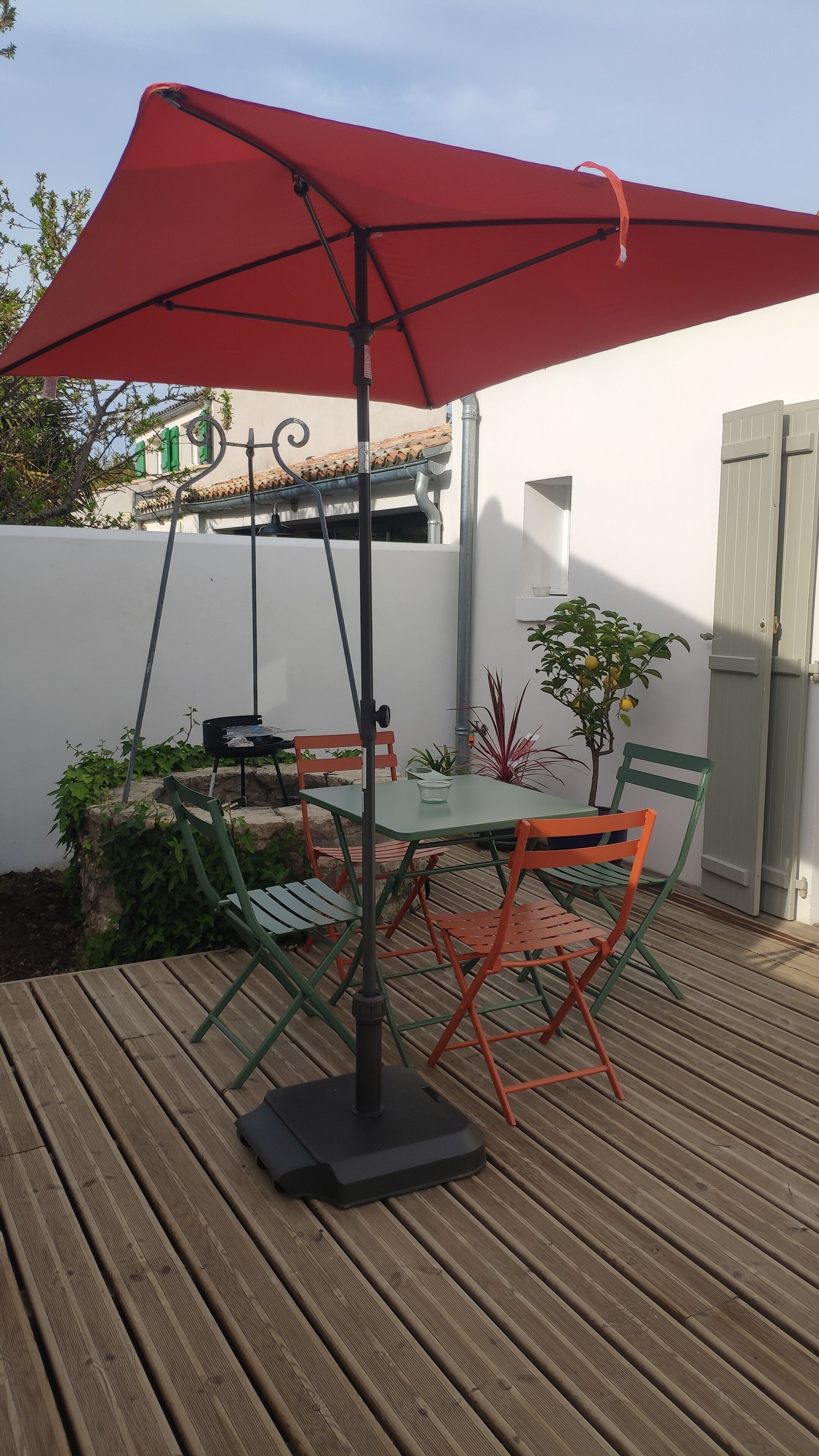 A wooden deck with a table and chairs under a red umbrella.