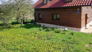 Una baita in legno con tetto in tegole rosse, fondamenta in pietra e un piccolo giardino con fiori gialli.