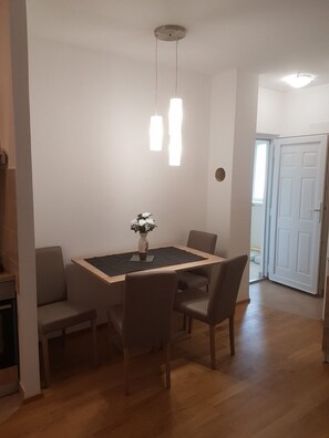 Een eethoek met een rechthoekige tafel, vier stoelen, een vaas met bloemen en hanglampen.