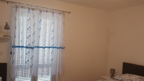 Une chambre avec deux lits, une fenêtre avec des rideaux à motifs, un luminaire au plafond et une table de chevet avec une lampe.