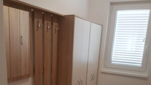 Une pièce dotée d’une armoire intégrée, d’un petit banc en bois avec des tiroirs et d’une fenêtre avec des stores.