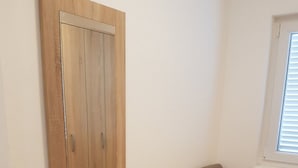 Una habitación con un armario de madera, una silla gris y una ventana con persianas.