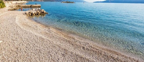 Uma praia de pedras com águas cristalinas e montanhas ao longe.