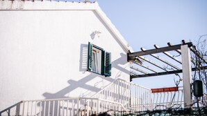 Un bâtiment blanc doté d’un balcon, d’une fenêtre avec des volets verts et d’une rambarde en métal.